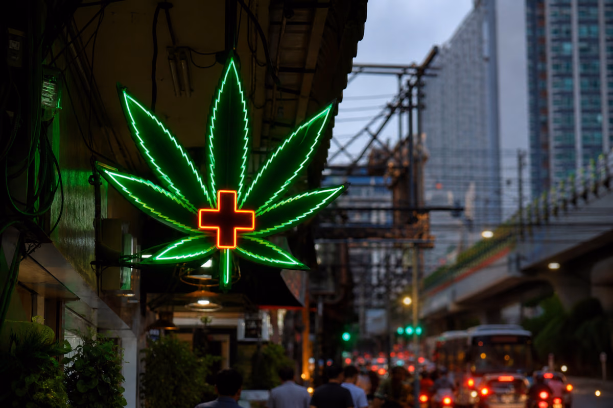 Neonbord in de vorm van een cannabisblad met medisch kruis boven een drukke straat in Bangkok